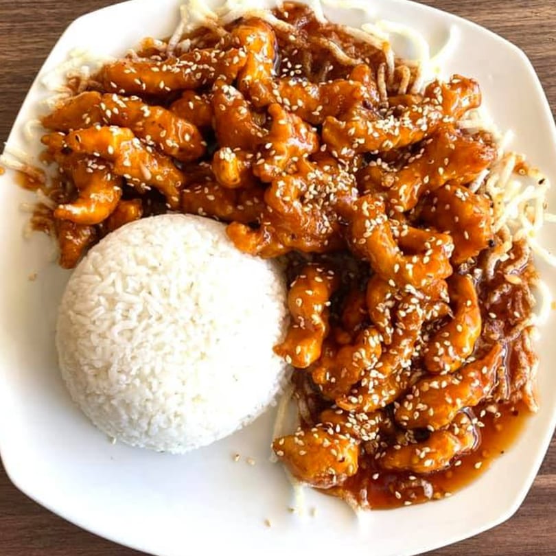 A white plate holds Saigon Terrace's sesame chicken with white rice and noodles.