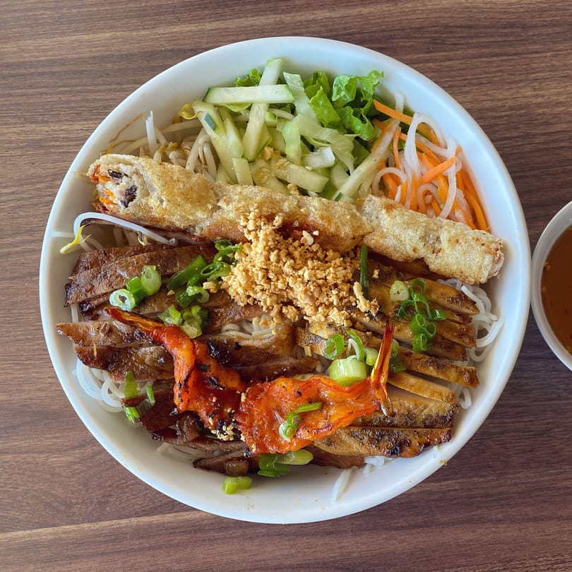 Vietnamese vermicelli bowl with grilled pork, shrimp, egg roll, and fresh vegetables.