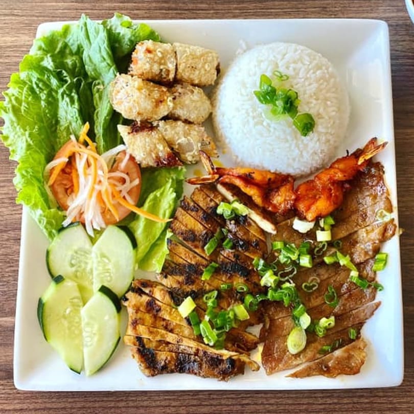 Vietnamese grilled pork, shrimp, egg rolls, rice, and fresh vegetables on a white plate.