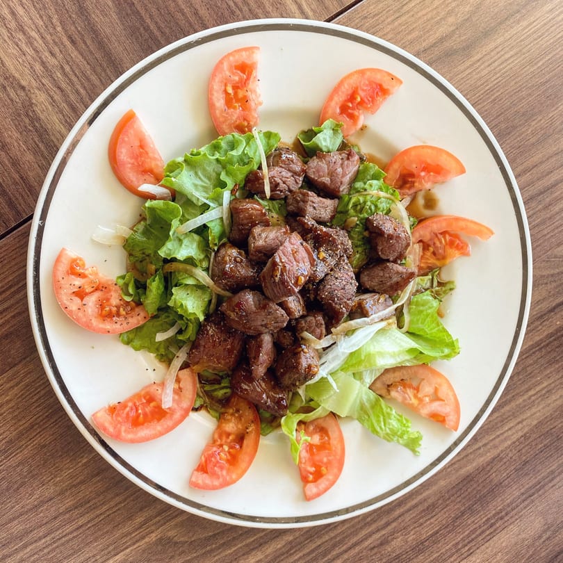 Vietnamese shaking beef salad with lettuce, tomatoes, and onions on a white plate.